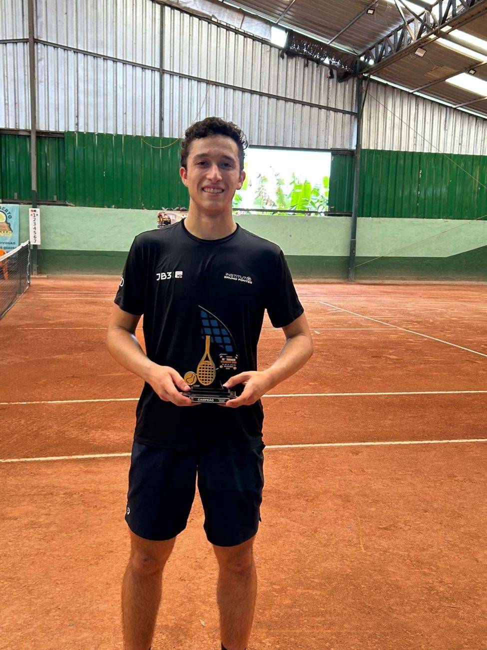 Bernardo Galvão com troféu em quadra de saibro, vestindo a camisa do Instituto e da JB3