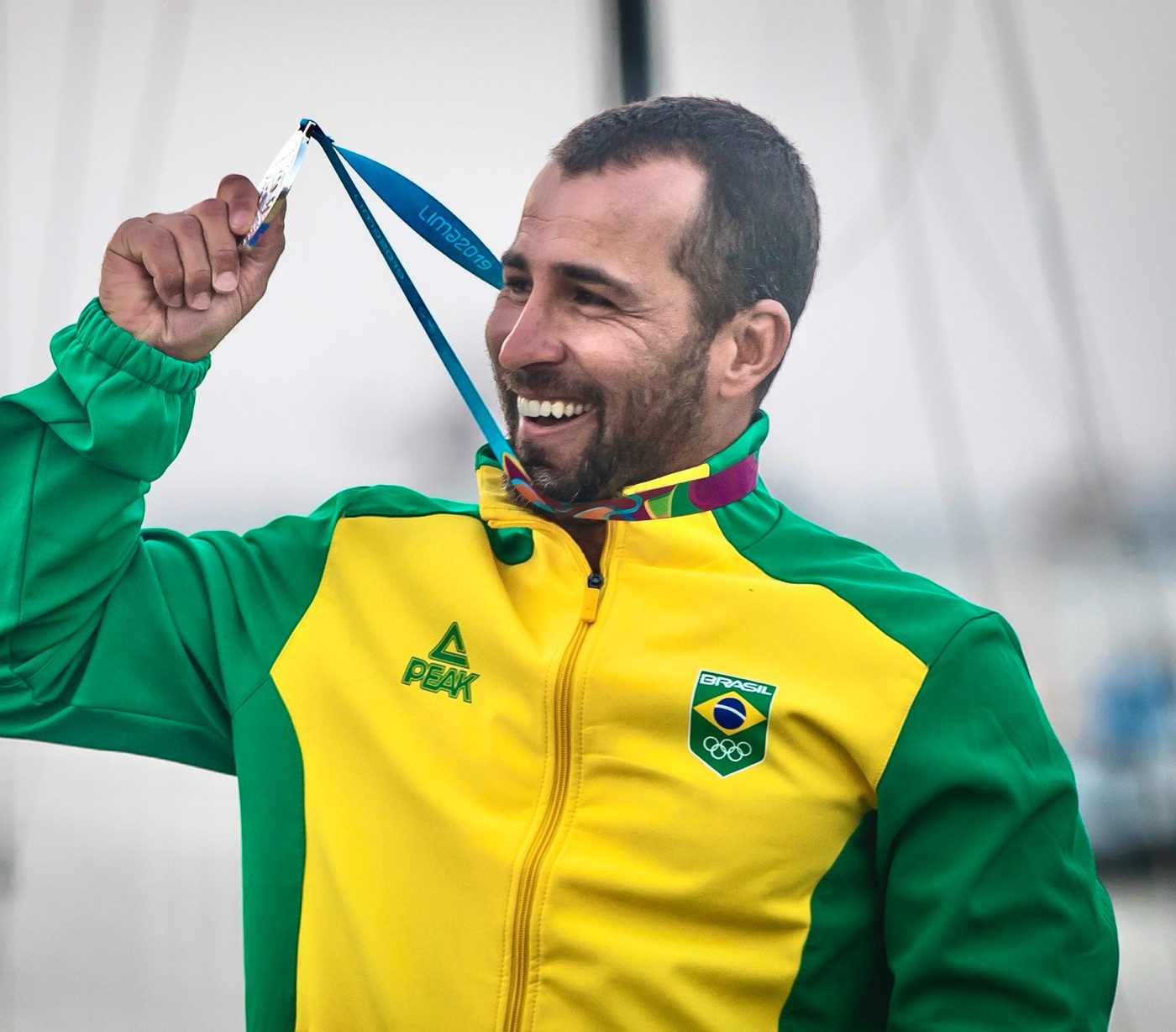 Bruno Fontes sorrindo e erguendo a medalha de prata dos Jogos Pan-Americanos de Lima 2019, com o agasalho do Brasil